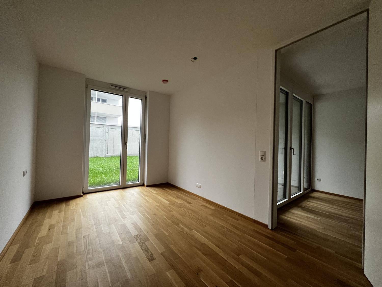 Lichtdurchfluteter Raum mit Holzboden und Zugang zu einem kleinen Gartenbereich.