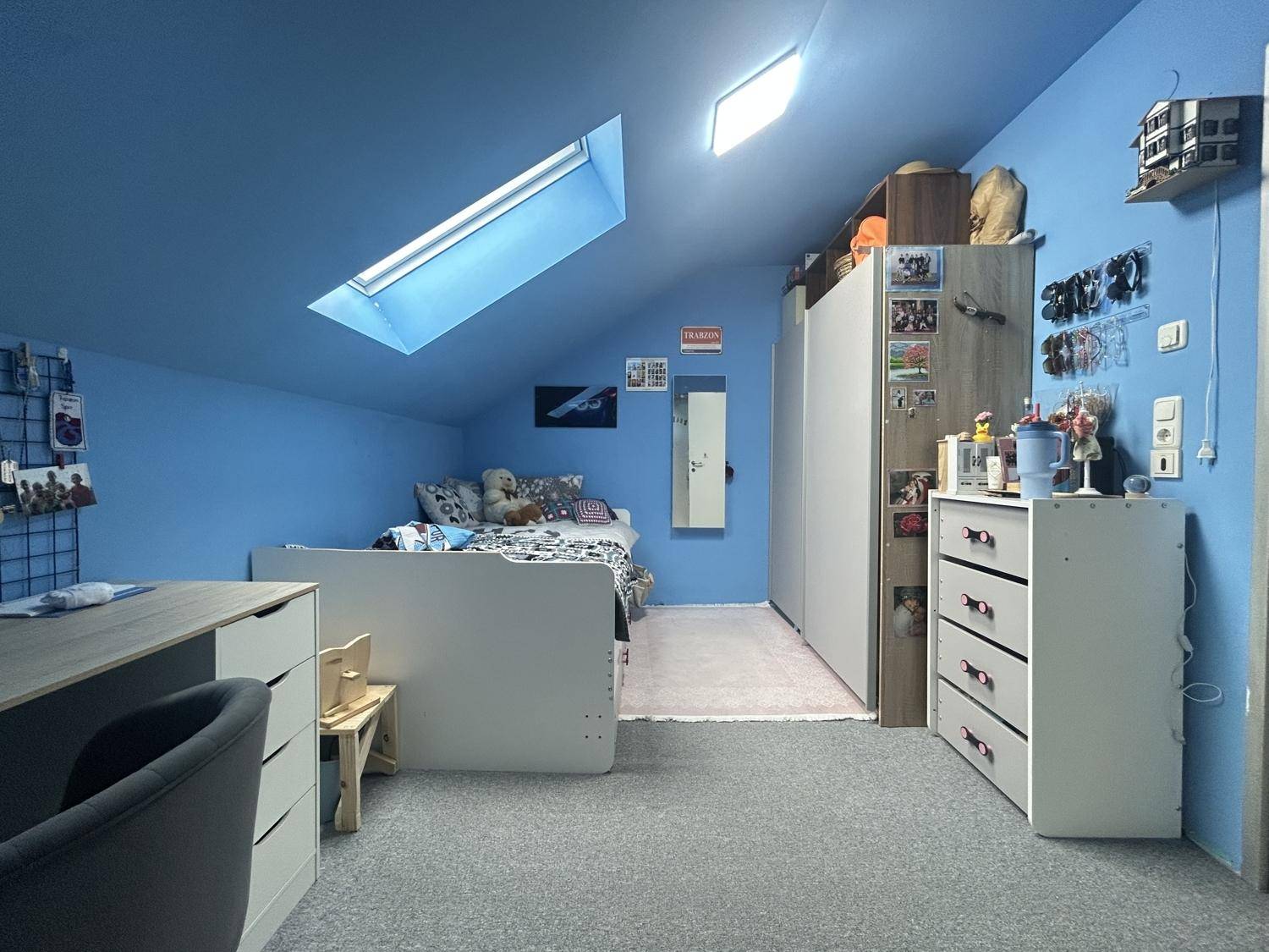Kinderzimmer im Dachgeschoss mit blauen Wänden, Dachfenster und Stauraum, hell und freundlich gestaltet.