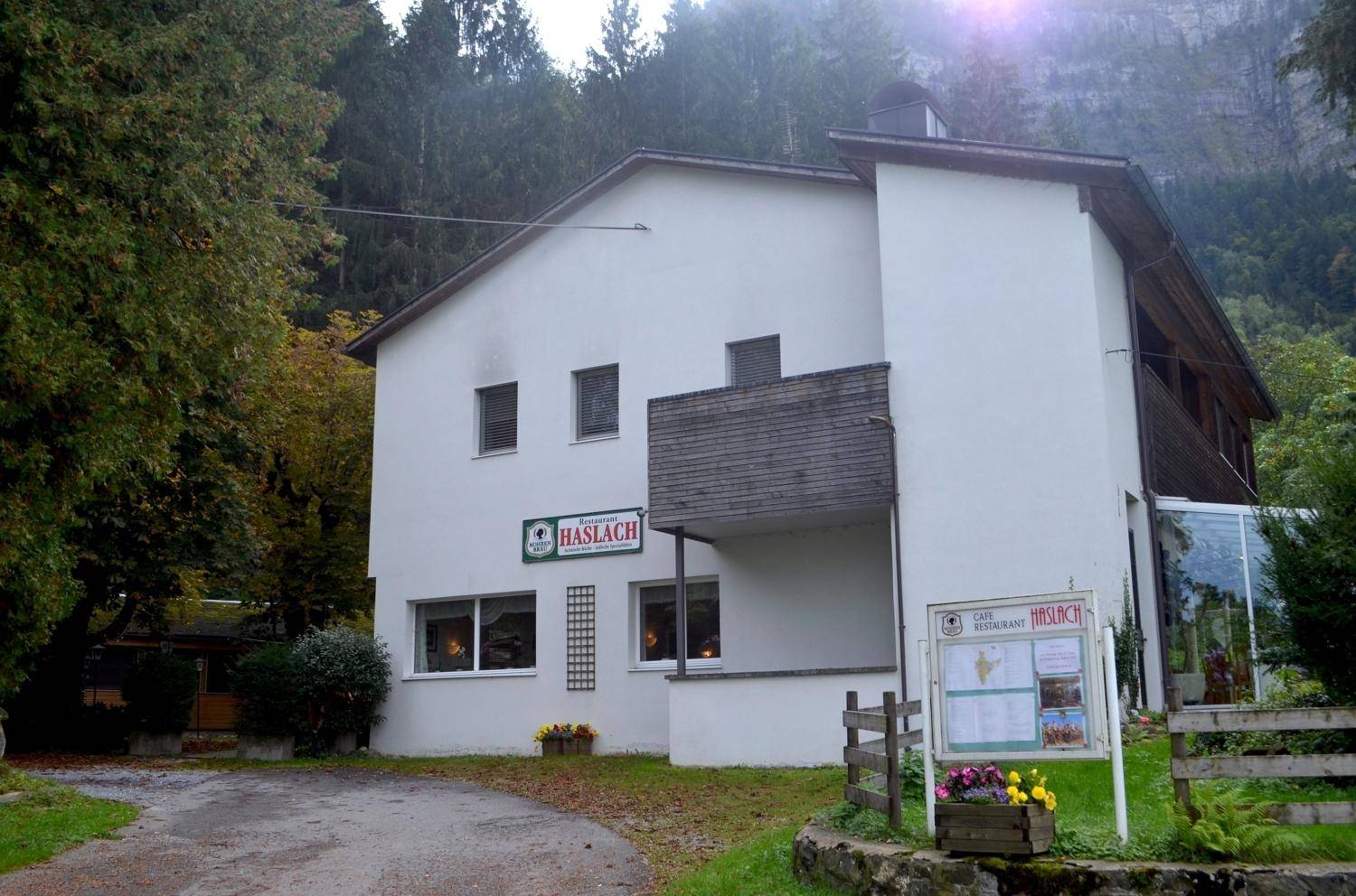 Außenansicht des Gasthofs Haslach, umgeben von Bäumen und Bergen im Hintergrund.