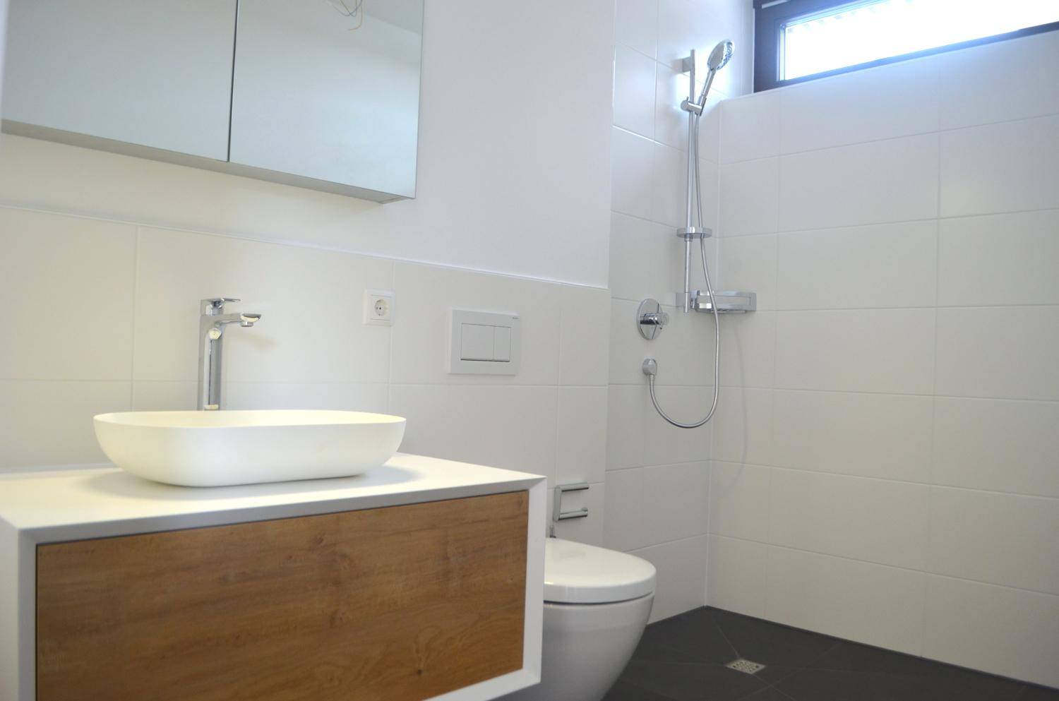 Modernes Badezimmer mit weißen Fliesen, Aufsatzwaschbecken, wandhängendem WC und Duschbereich.