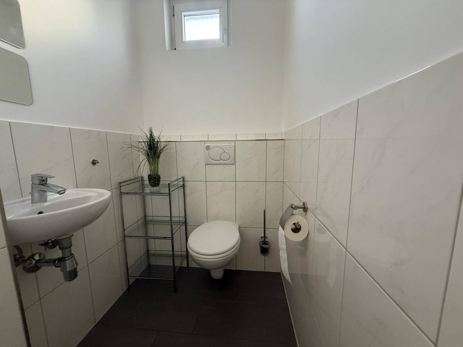 Separates Gäste-WC mit wandhängender Toilette, kleinem Waschbecken und Fenster.