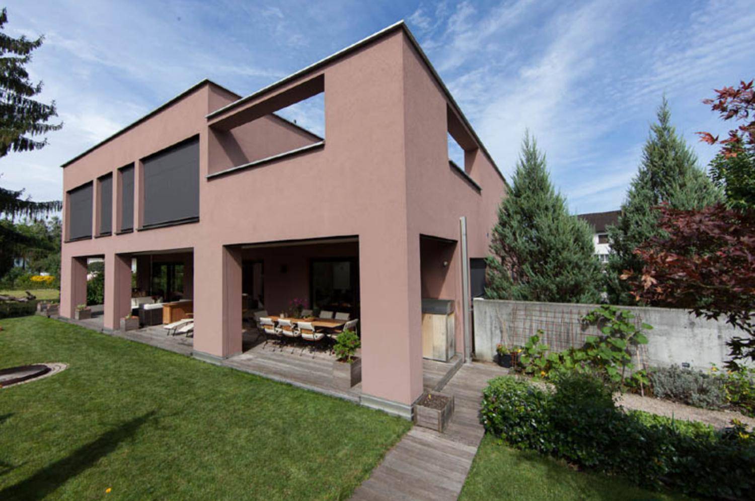 Seitliche Ansicht des Hauses mit großer Rasenfläche und einer möblierten Holzterrasse.