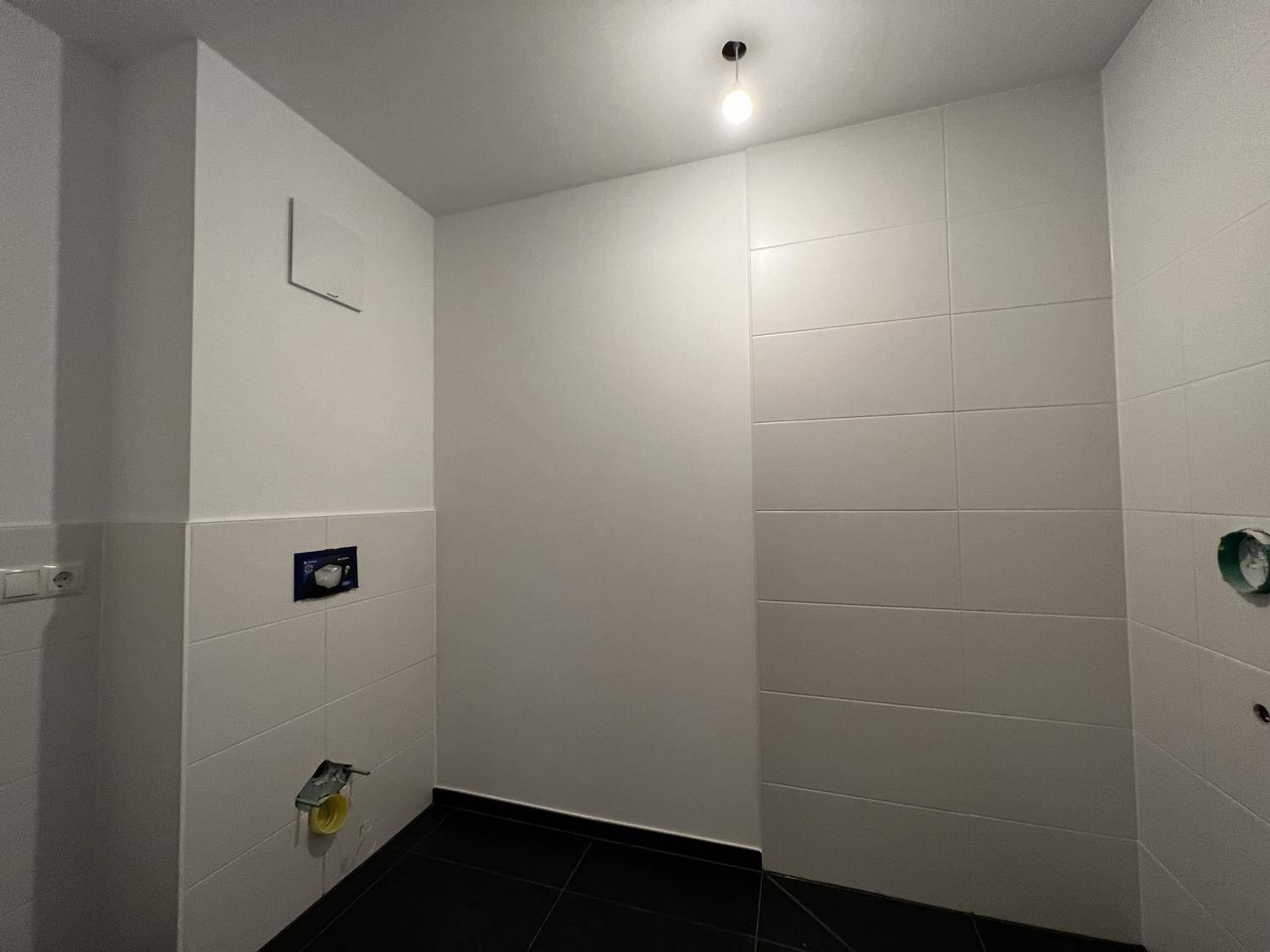 Unfertiges Badezimmer mit weißen Wandfliesen und dunklem Boden, bereit für die Installation der Sanitärobjekte.