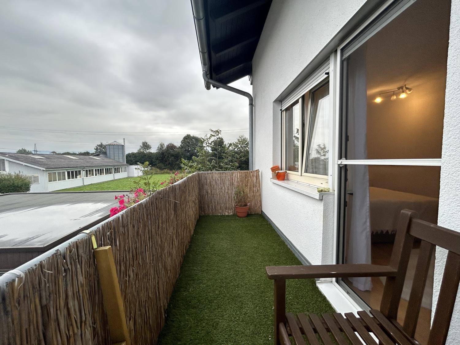 Schmaler Balkon mit Kunstrasen, Bambusverkleidung und einem Stuhl, ideal für eine kleine Auszeit.