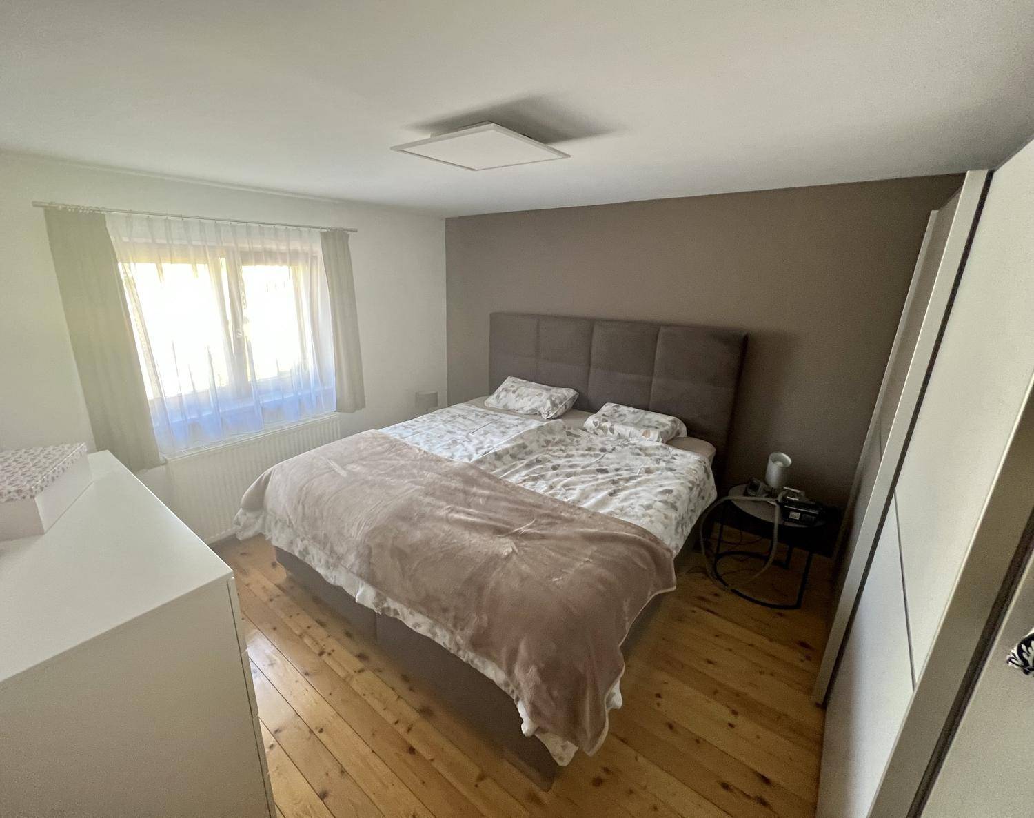 Gemütliches Schlafzimmer mit Holzboden, Doppelbett und großem Fenster für viel Tageslicht.