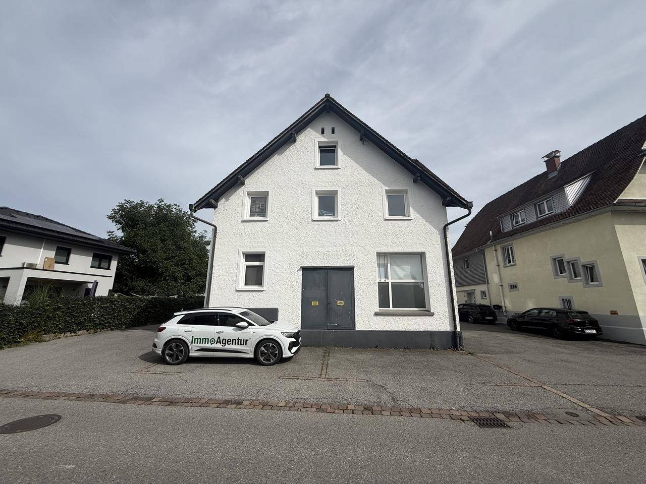 Vorderansicht des weißen Gebäudes mit einem geparkten Auto und großem Vorplatz.