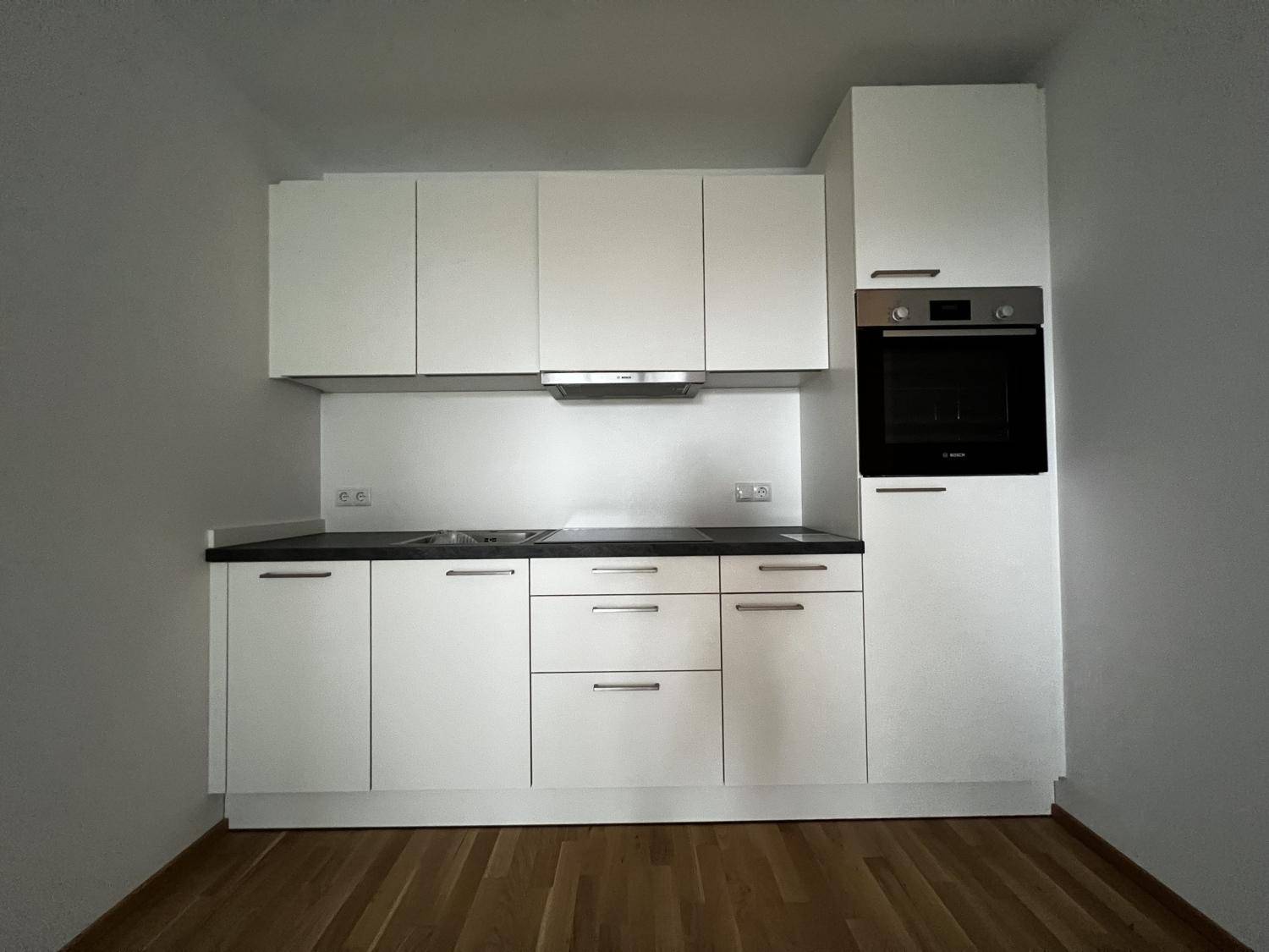 Neue, moderne Einbauküche in Weiß mit integriertem Backofen und dunkler Arbeitsplatte.