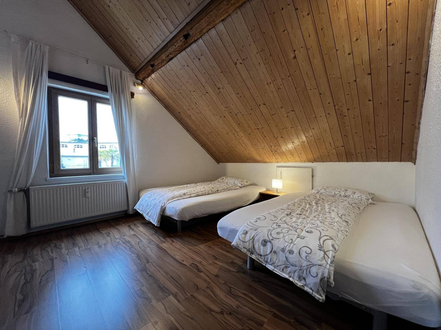 Helles Schlafzimmer im Dachgeschoss mit zwei Einzelbetten, Holzbalken und Fenster.