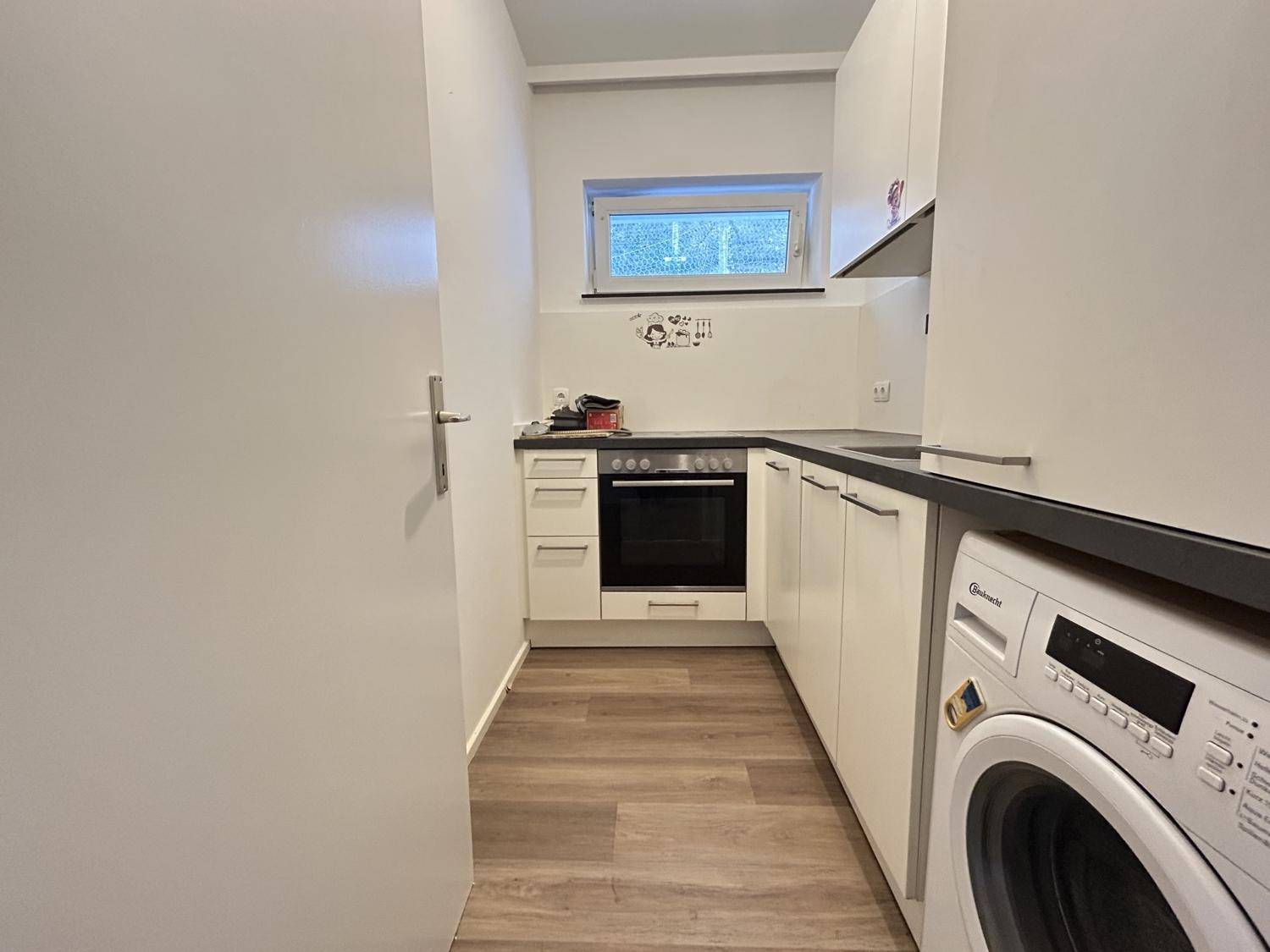Funktionale Küche mit Einbaugeräten, Waschmaschine und Fenster für Tageslicht.