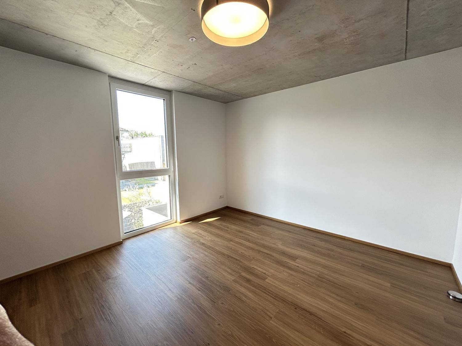 Geräumiges Schlafzimmer mit hellem Holzfußboden und großem Fenster für viel Tageslicht.