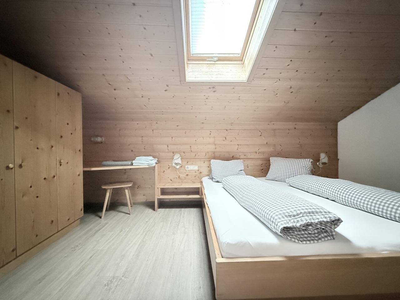Gemütliches Schlafzimmer mit Holzverkleidung, Dachfenster und schlichtem Doppelbett.