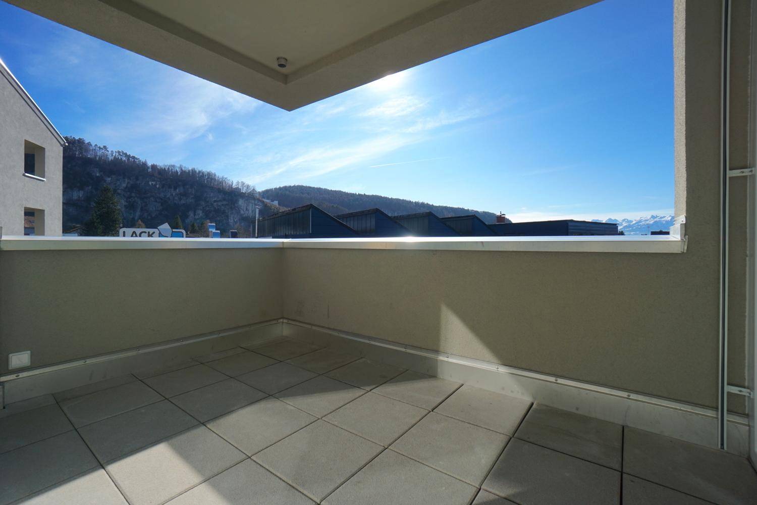 Sonniger Balkon mit Fliesenboden und einem weiten Blick auf die umliegende Berglandschaft.