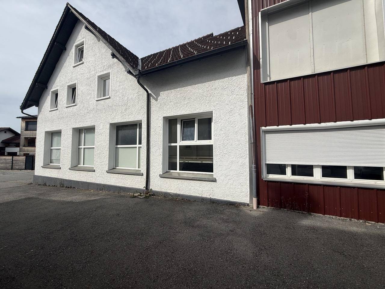 Seitenansicht des Gebäudes mit weiß verputzter Fassade und angrenzendem roten Anbau.