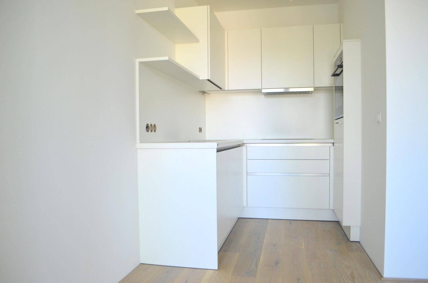 Helle, moderne Küche mit weißen Schränken, integrierten Geräten und hellem Holzfußboden.