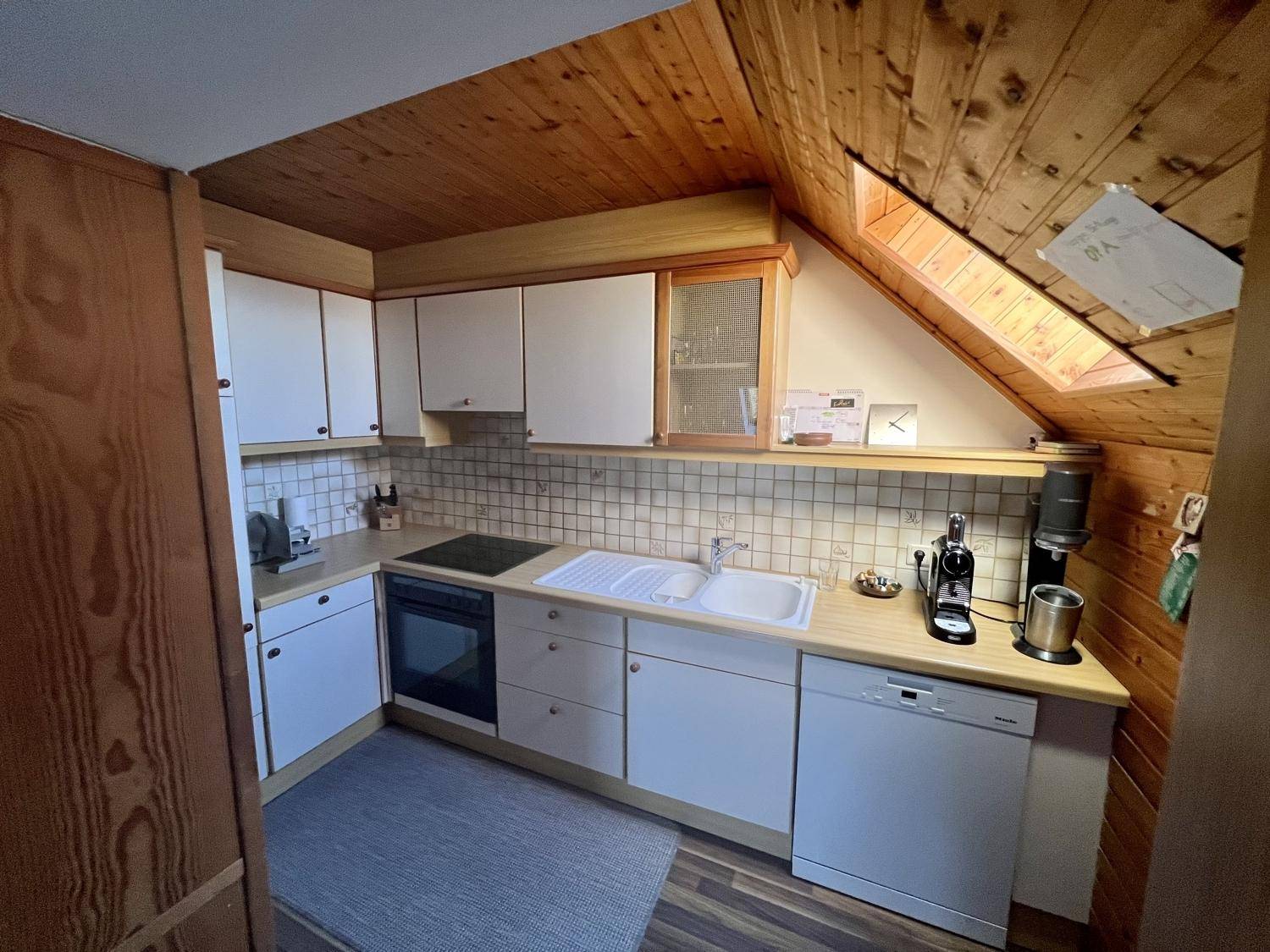 Funktionale Küche mit Dachschräge, Holzwänden und Einbaugeräten unter einem Dachfenster.