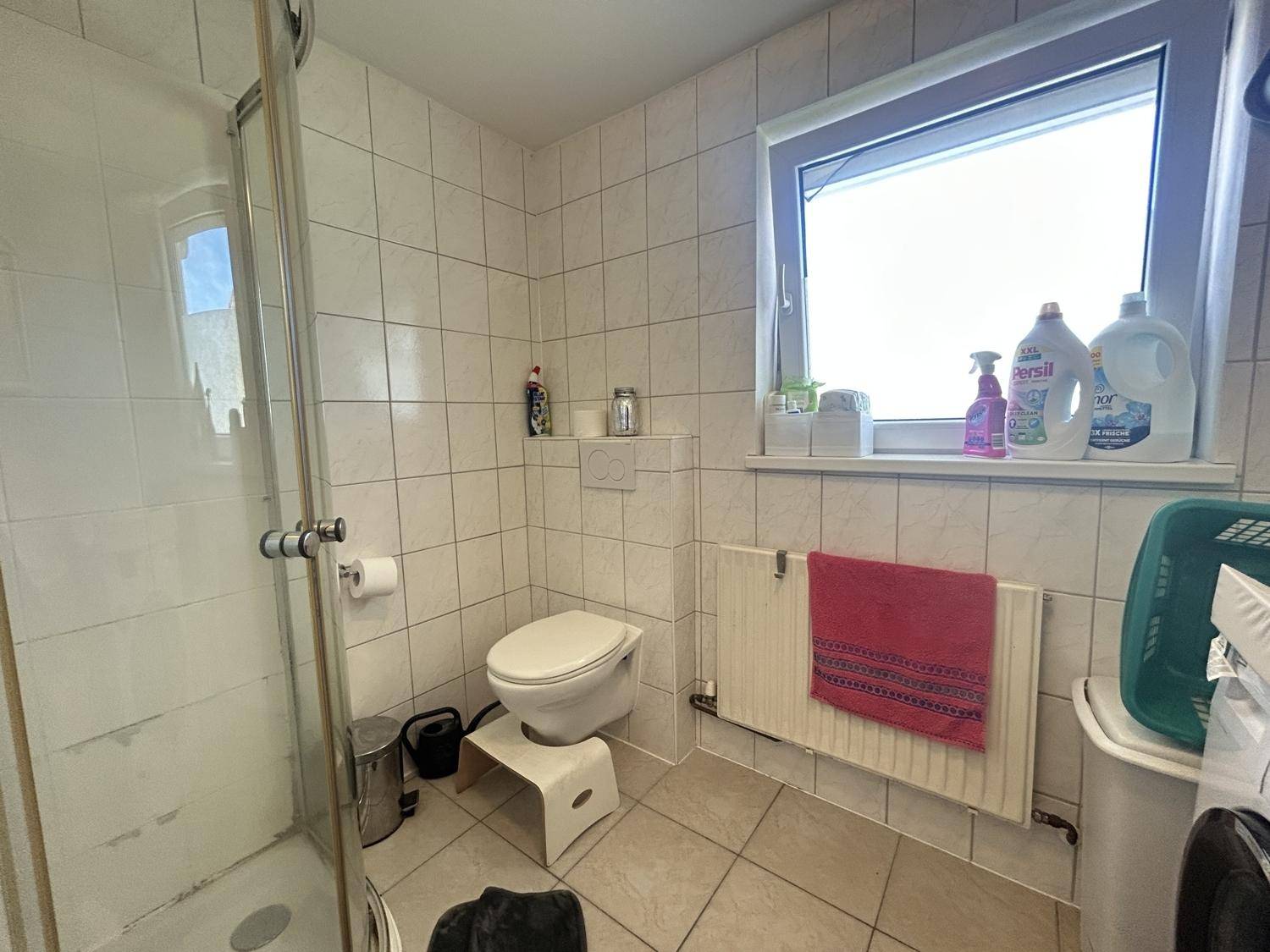 Gefliestes Badezimmer mit Duschkabine, WC und Fenster, hell und praktisch eingerichtet.
