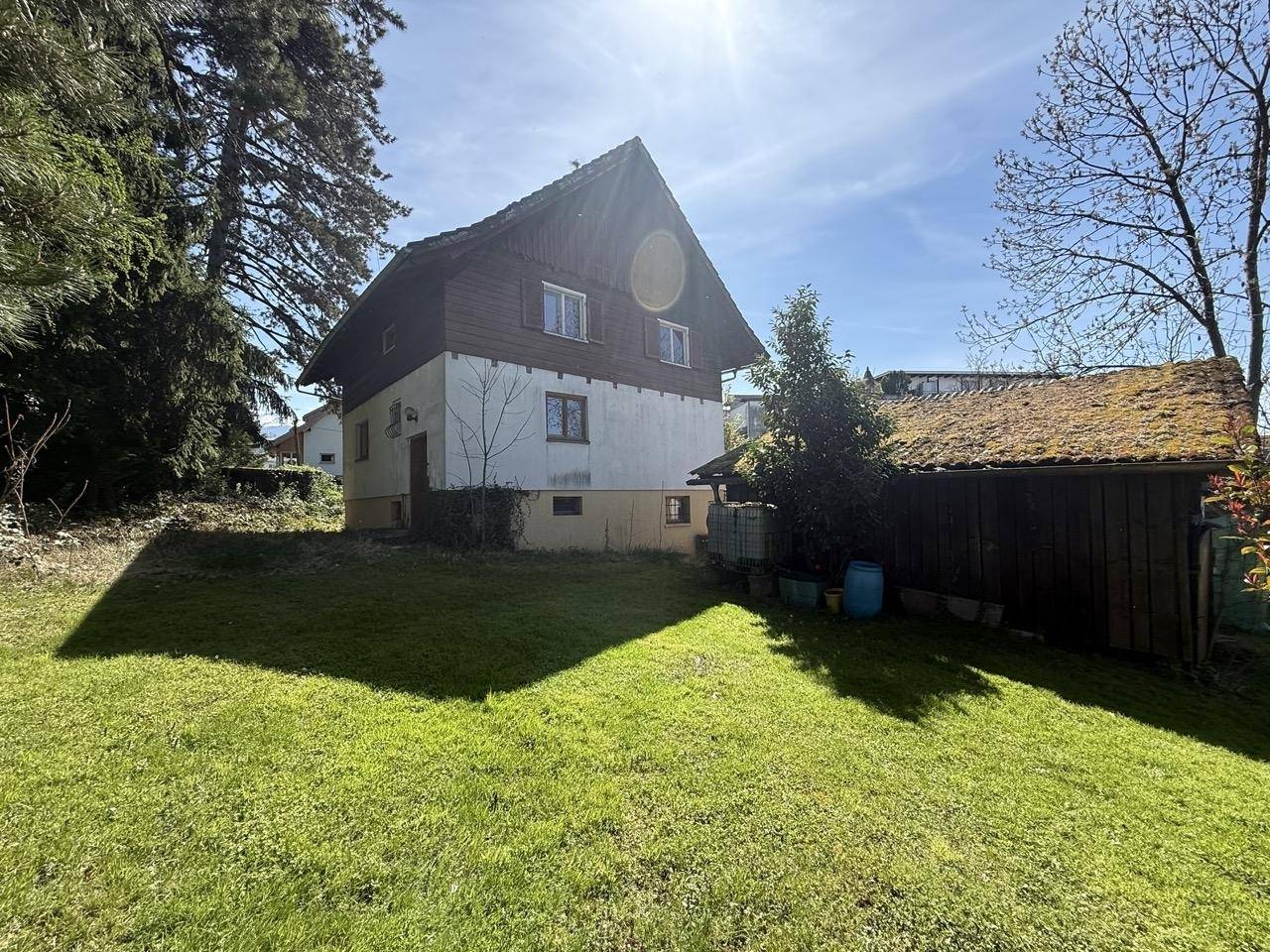 Sonniger Garten mit Rasenfläche und Blick auf das Wohnhaus und ein Nebengebäude.