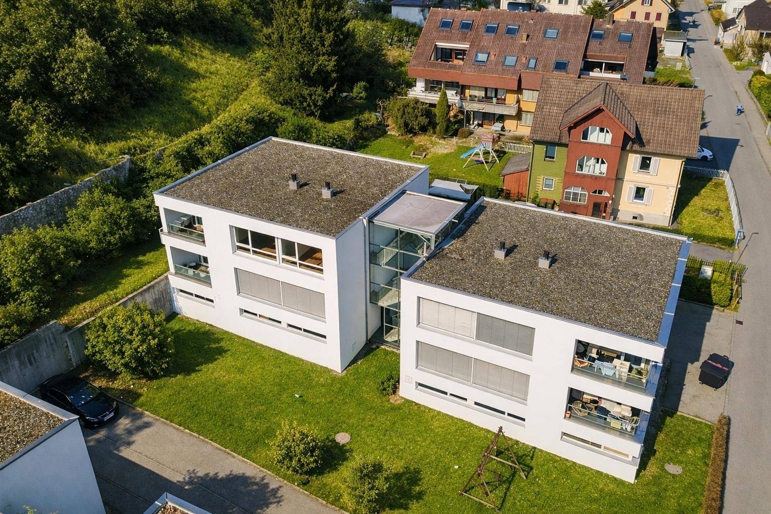 Luftaufnahme eines modernen Wohnkomplexes mit weißer Fassade und Flachdächern in grüner Umgebung.
