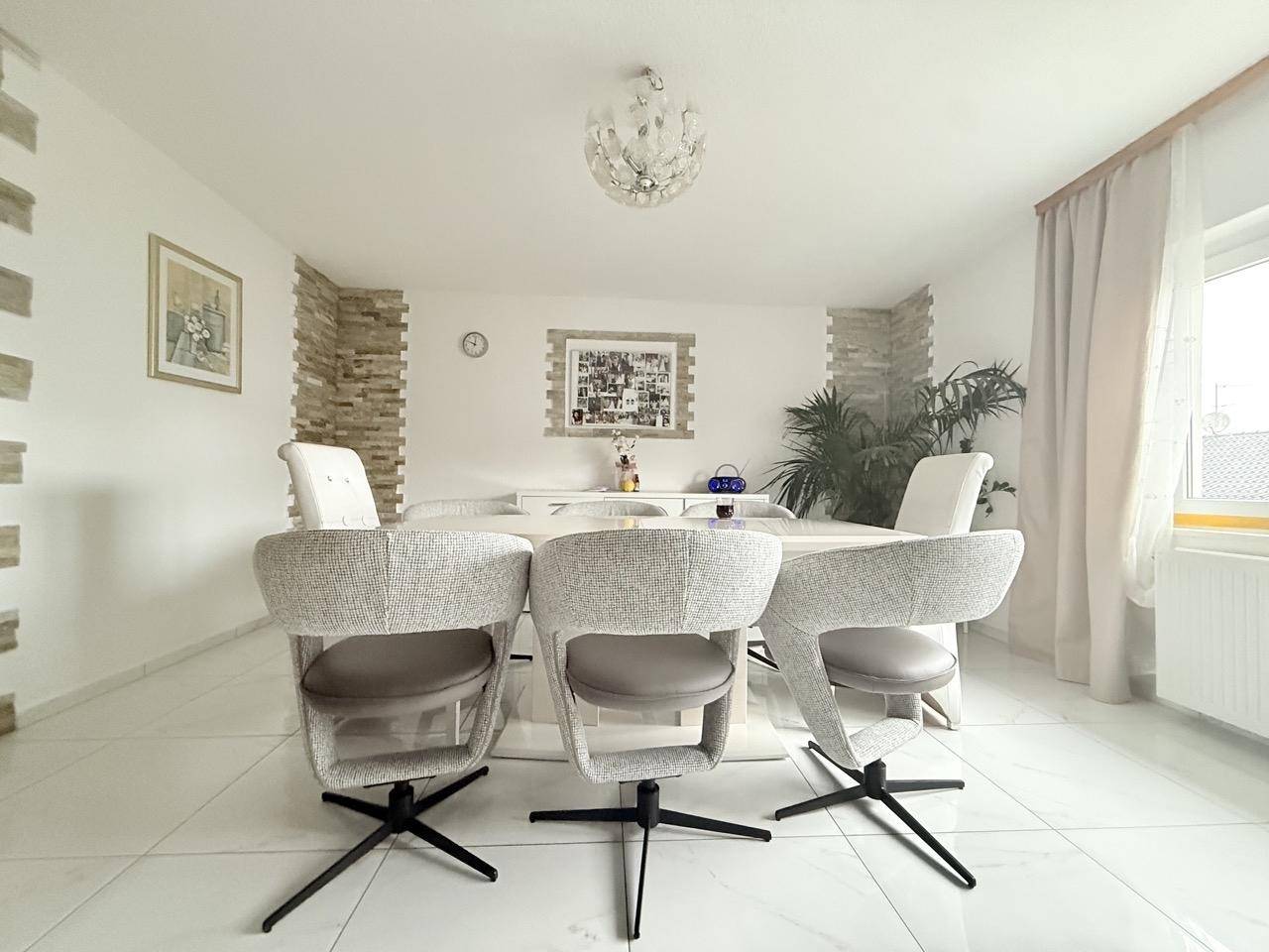 Eleganter Essbereich mit großem weißen Tisch, modernen Stühlen und Fliesenboden.
