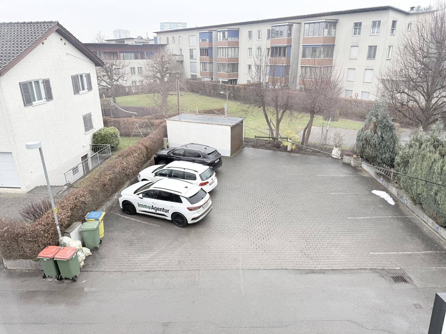 Großer gepflasterter Parkplatz mit mehreren Autos und angrenzenden Gebäuden.
