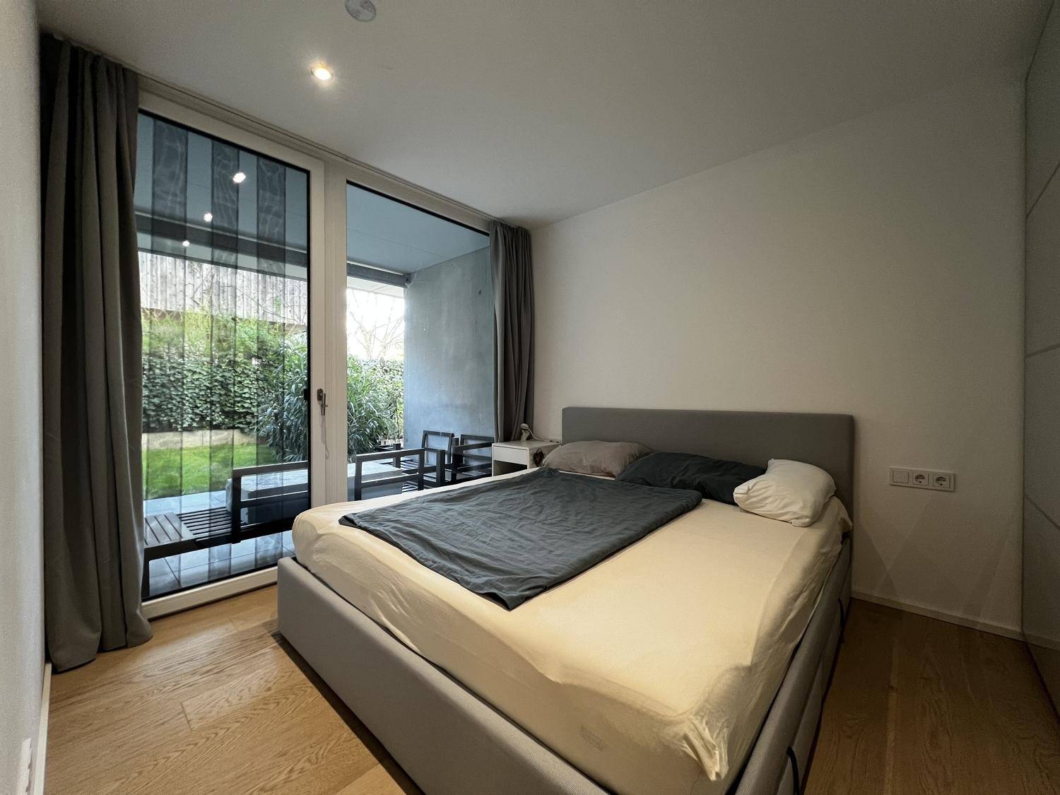 Helles Schlafzimmer mit Holzboden, großem Bett und direktem Zugang zur Terrasse oder zum Garten.