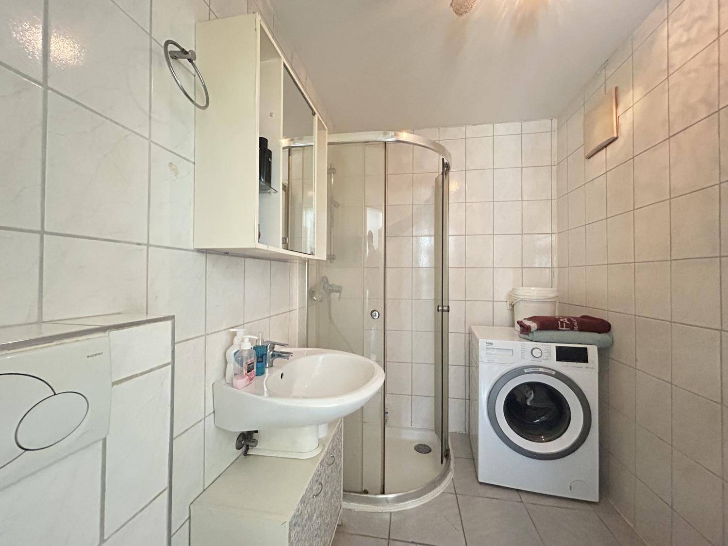 Funktionales Badezimmer mit Duschkabine, Waschbecken, WC und Waschmaschine, komplett gefliest.
