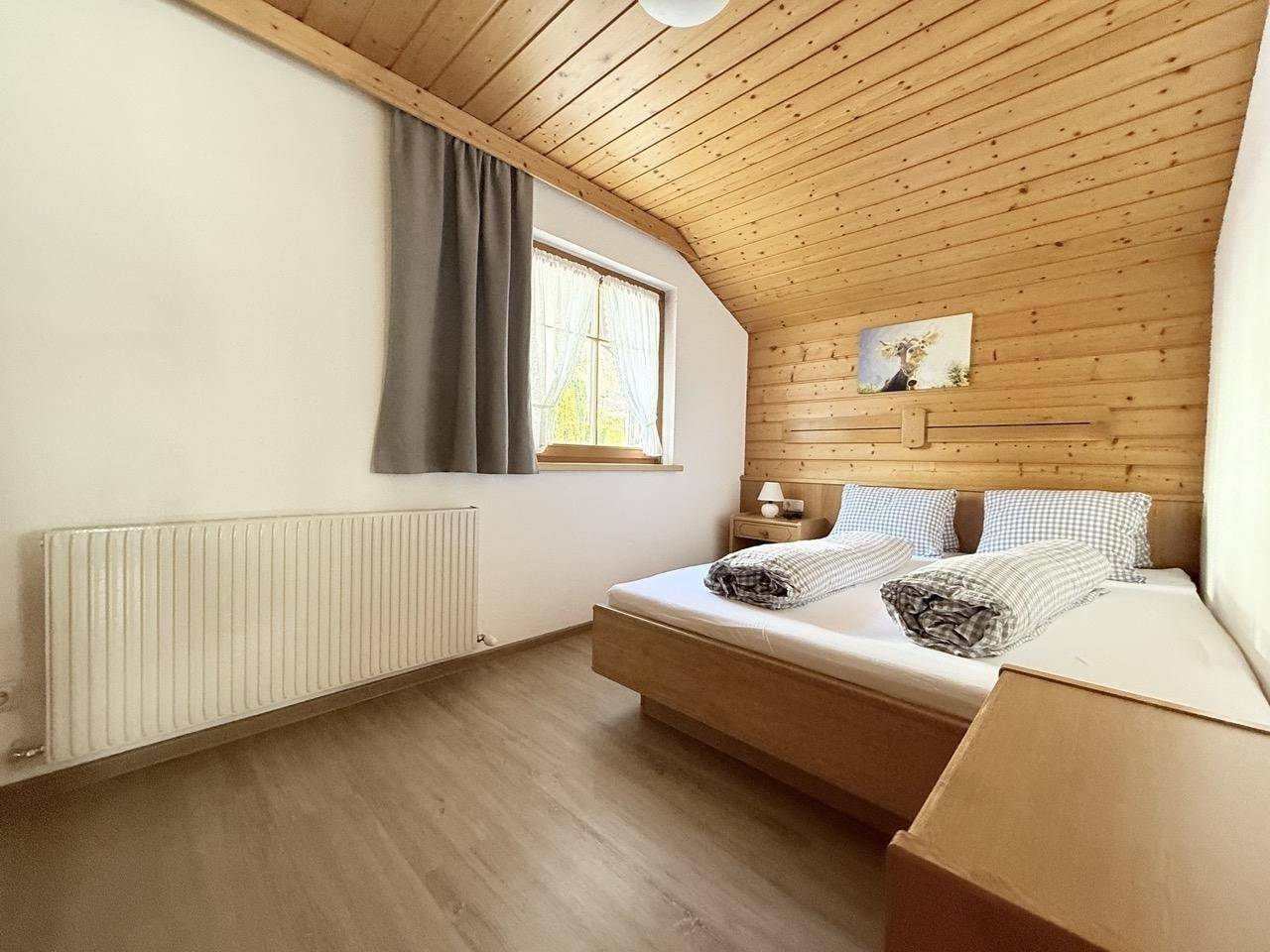 Rustikales Schlafzimmer mit Holzverkleidung, Doppelbett und Fenster mit Blick ins Grüne.