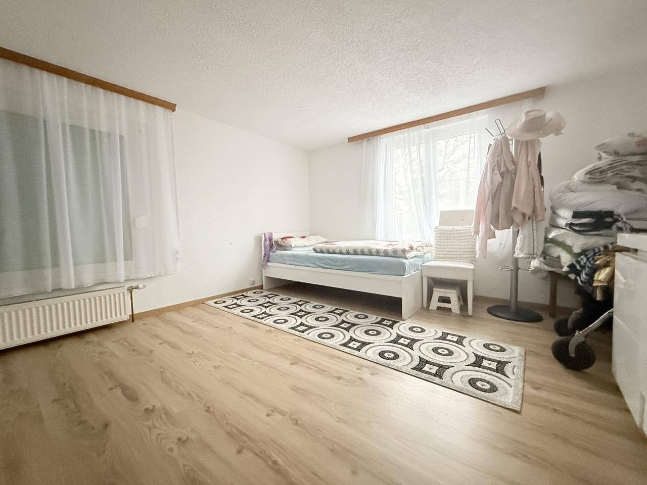 Helles Schlafzimmer mit Holzboden, einem Bett und großem Fenster.