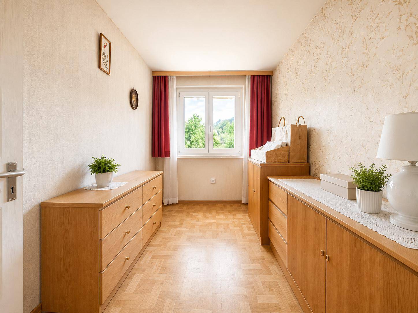 Schmaler Raum mit Holzkommoden, Laminatboden und Fenster mit rotem Vorhang.