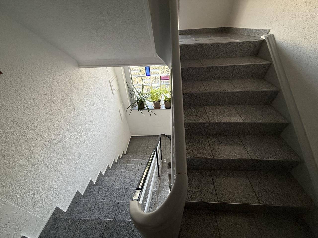 Treppenhaus mit gefliesten Stufen, Geländer und einem Buntglasfenster.