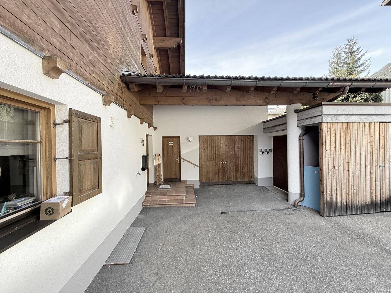 Eingangsbereich des Hauses mit überdachtem Carport und Holztoren zur Garage.
