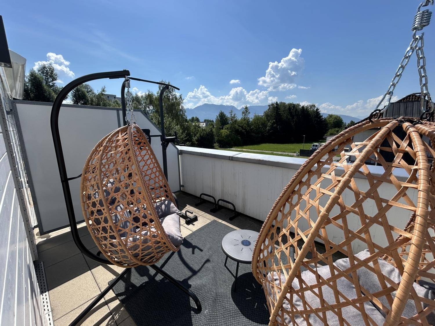 Sonniger Balkon mit Hängesesseln und weitem Blick auf die umliegende Landschaft und Berge.
