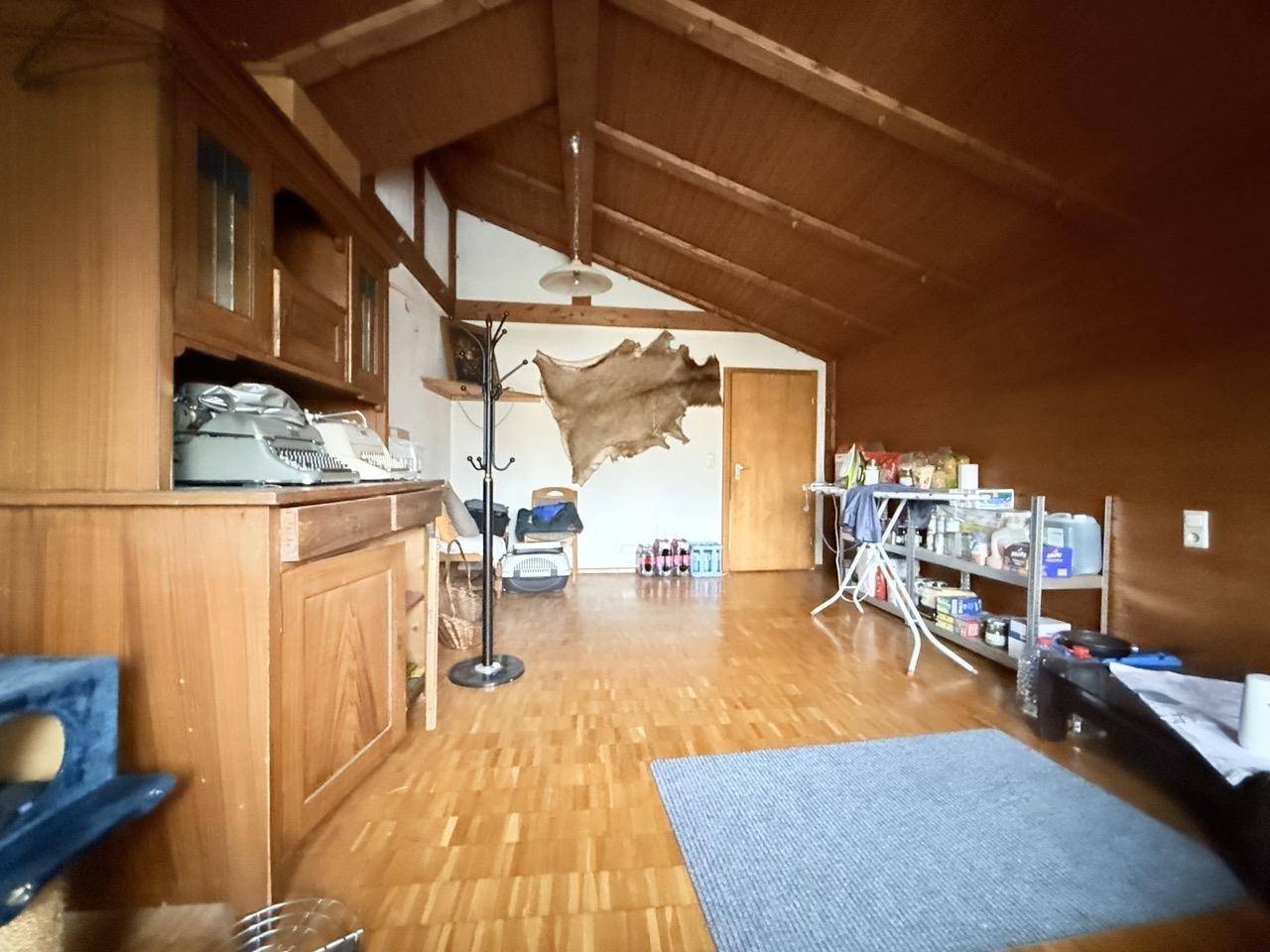 Geräumiges Dachzimmer mit Holzvertäfelung, sichtbaren Balken und Dachschräge, vielseitig nutzbar.