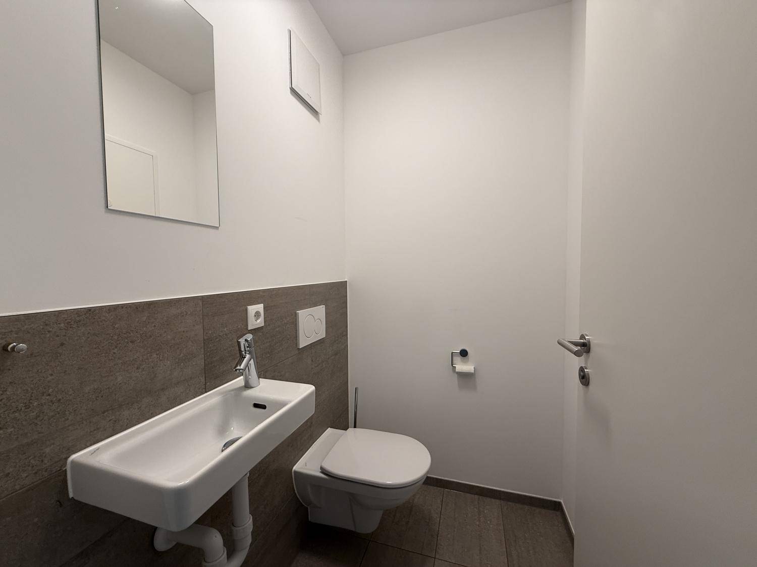 Modernes Gäste-WC mit Wand-WC, Waschbecken und Spiegel, in neutralen Farbtönen gehalten.