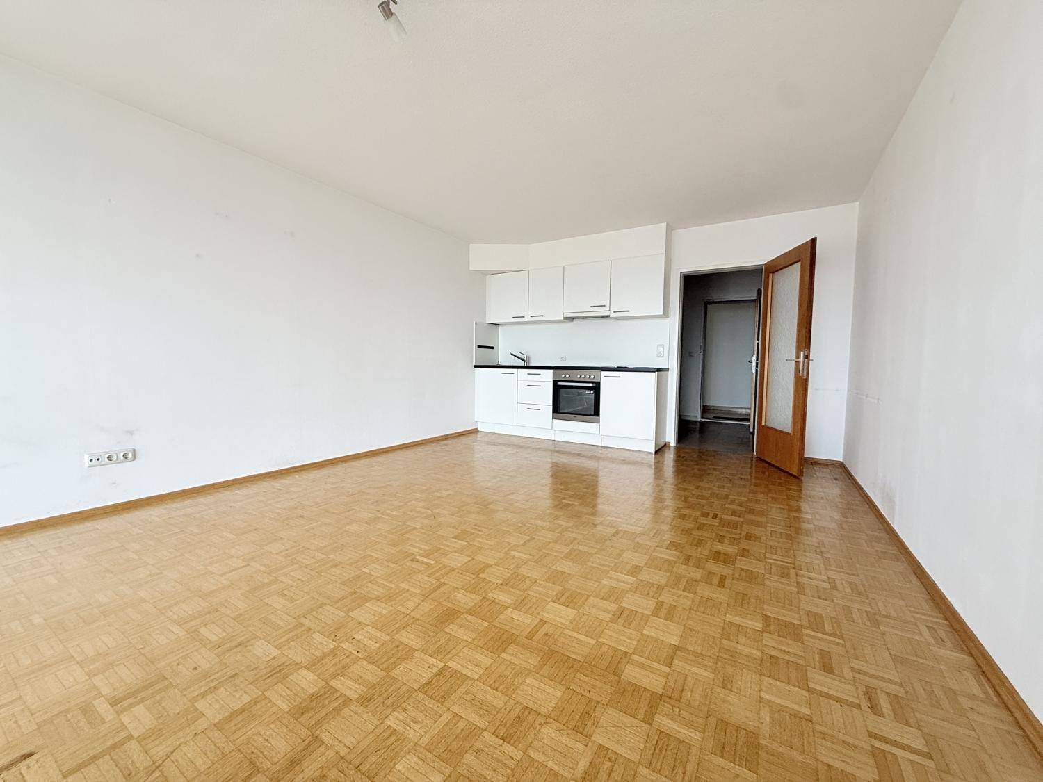 Geräumiger Wohnbereich mit integrierter Küchenzeile und klassischem Parkettboden, ideal für offenes Wohnen.