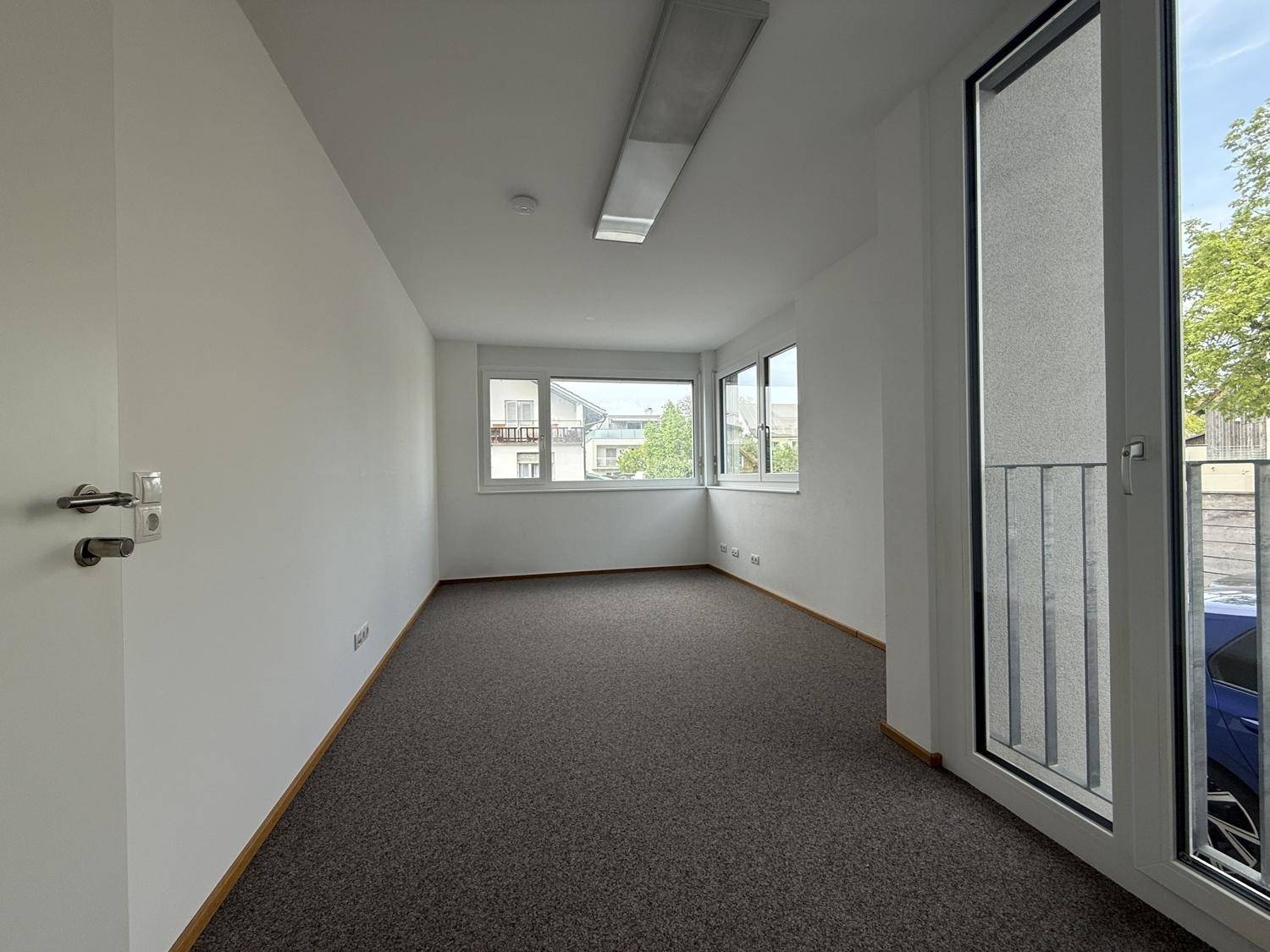 Heller Büroraum mit Teppichboden und großen Fenstern, die viel Tageslicht hereinlassen.