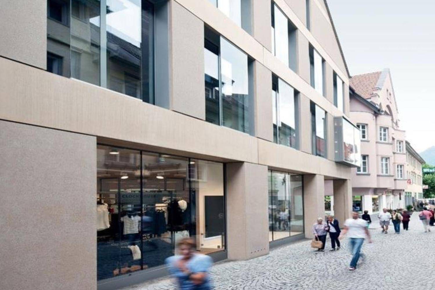 Belebte Einkaufsstraße mit Kopfsteinpflaster und modernen Ladenfronten eines Geschäftsgebäudes.