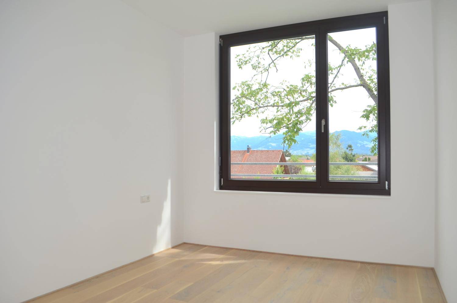 Helles Zimmer mit Holzboden und Fenster, das einen weiten Blick auf die Berge bietet.
