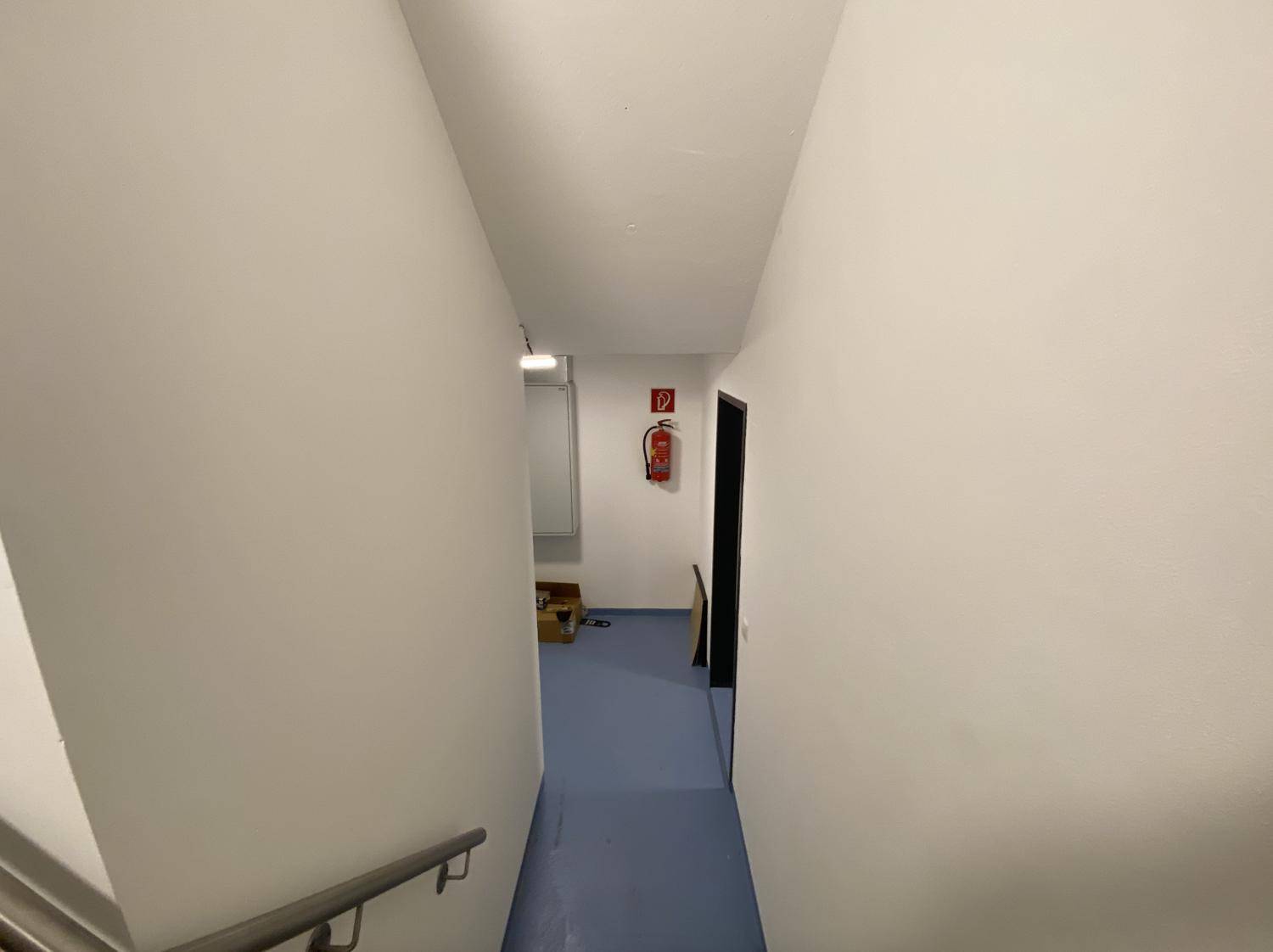 Langer, schlichter Flur mit glattem Vinylboden und weißen Wänden, der zu weiteren Räumen führt.