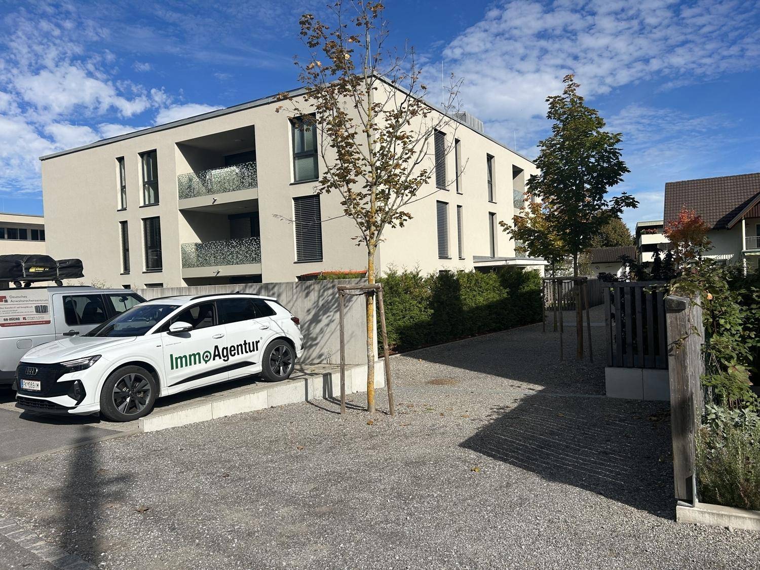 Neubau-Wohngebäude mit moderner Architektur, Balkonen und Außenparkplätzen an einem sonnigen Tag.