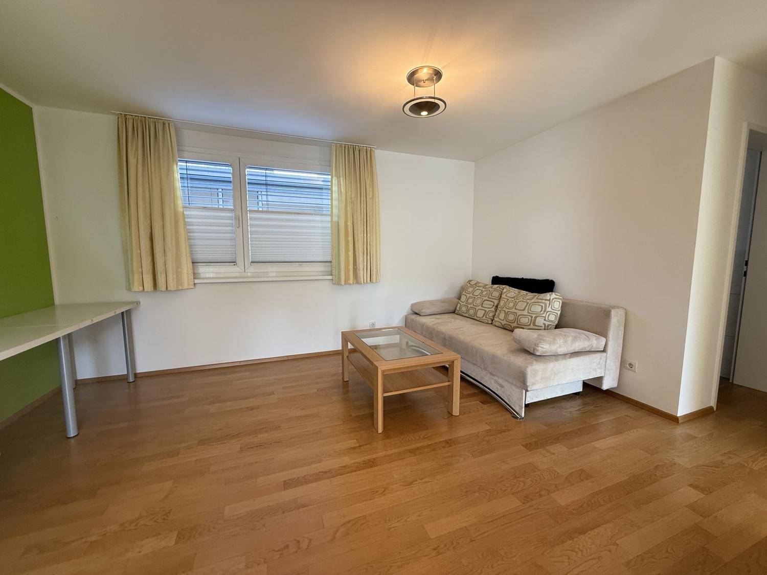 Gemütliches Wohnzimmer mit Holzboden, Sofa und einem Fenster mit Jalousien.