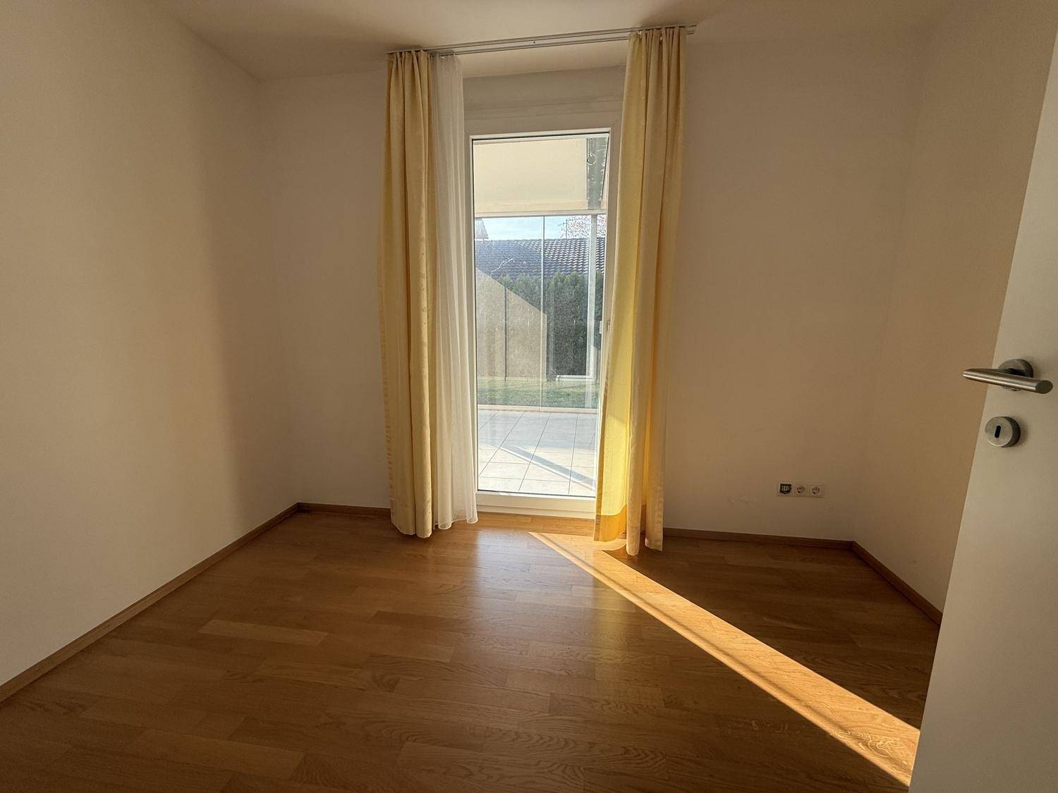 Helles Zimmer mit Holzboden und Zugang zu einem Außenbereich, ideal als Schlaf- oder Arbeitszimmer.
