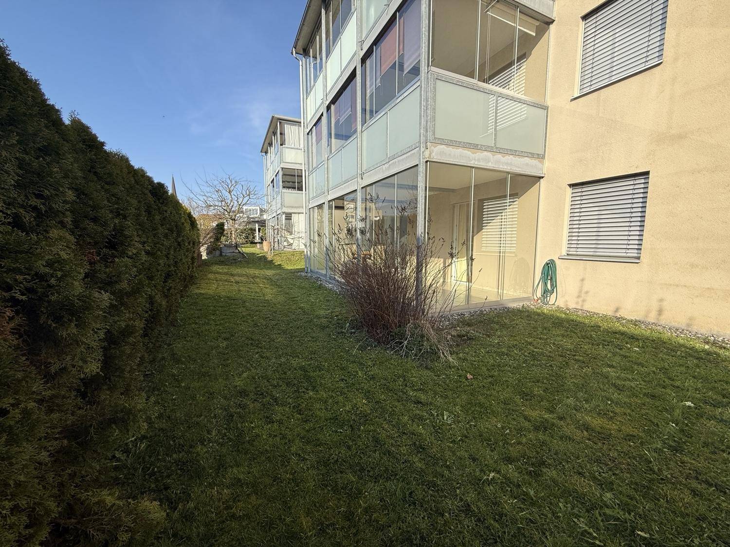 Außenansicht des Gebäudes mit gepflegtem Rasen und einer verglasten Terrasse im Erdgeschoss.