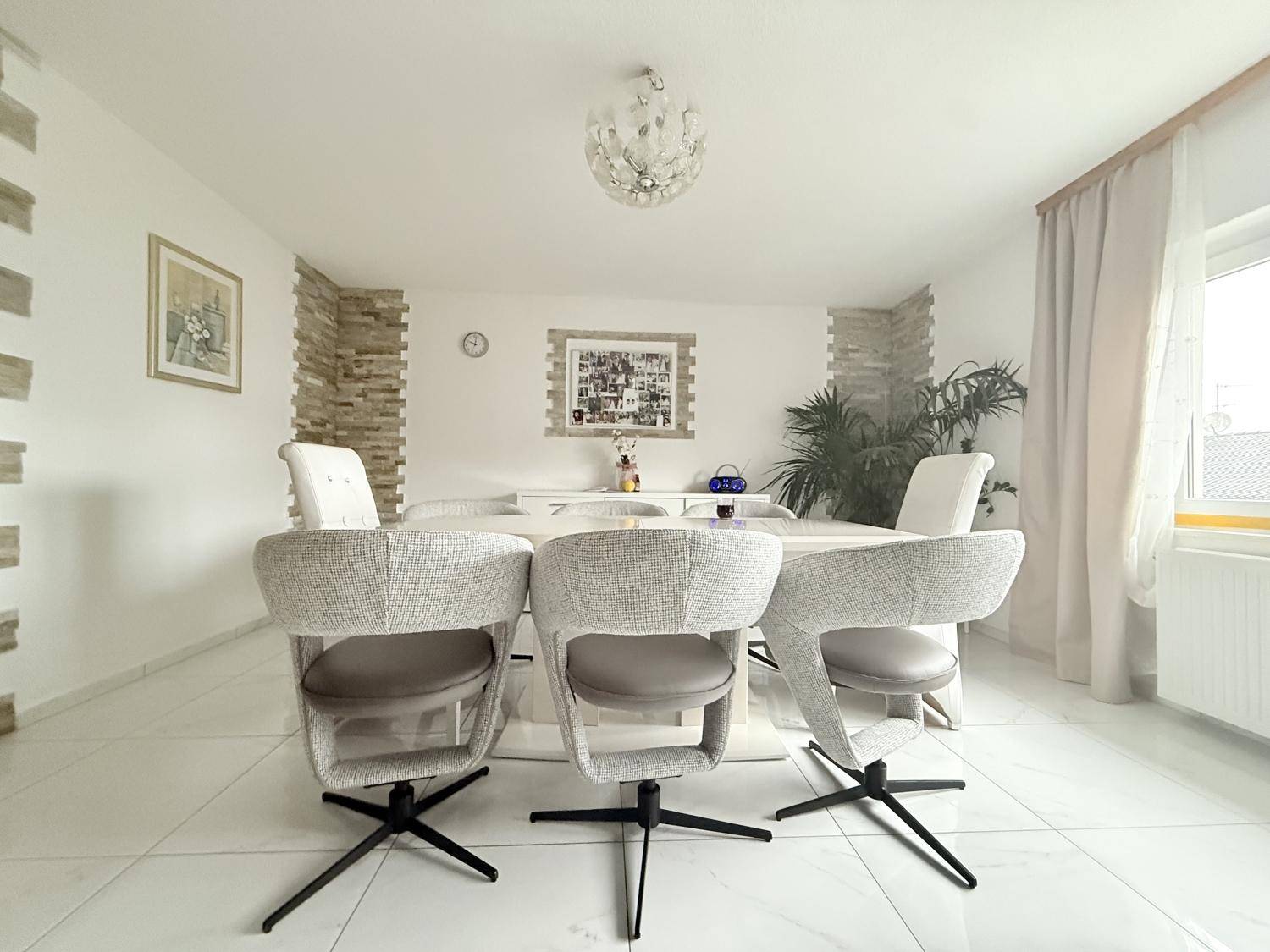 Eleganter Essbereich mit großem weißen Tisch, modernen Stühlen und Fliesenboden.