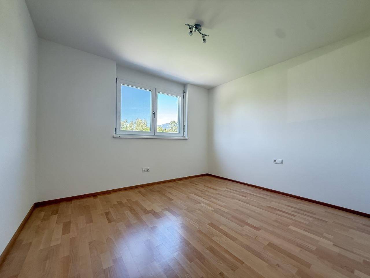 Freundliches Schlafzimmer mit Holzfußboden und einem Fenster, das viel Licht hereinlässt.