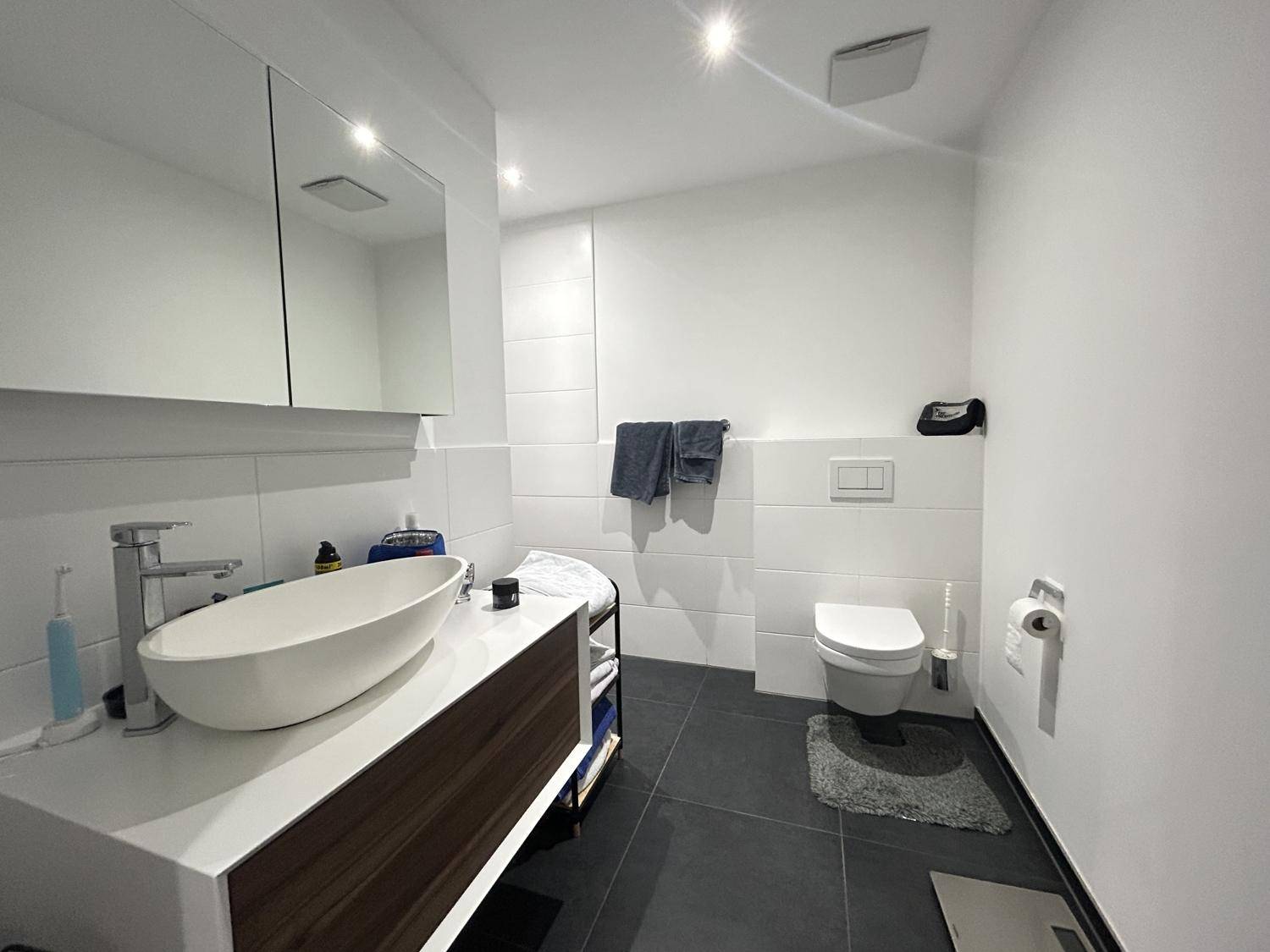 Modernes Badezimmer mit Waschtisch, Wand-WC und dunklen Bodenfliesen.