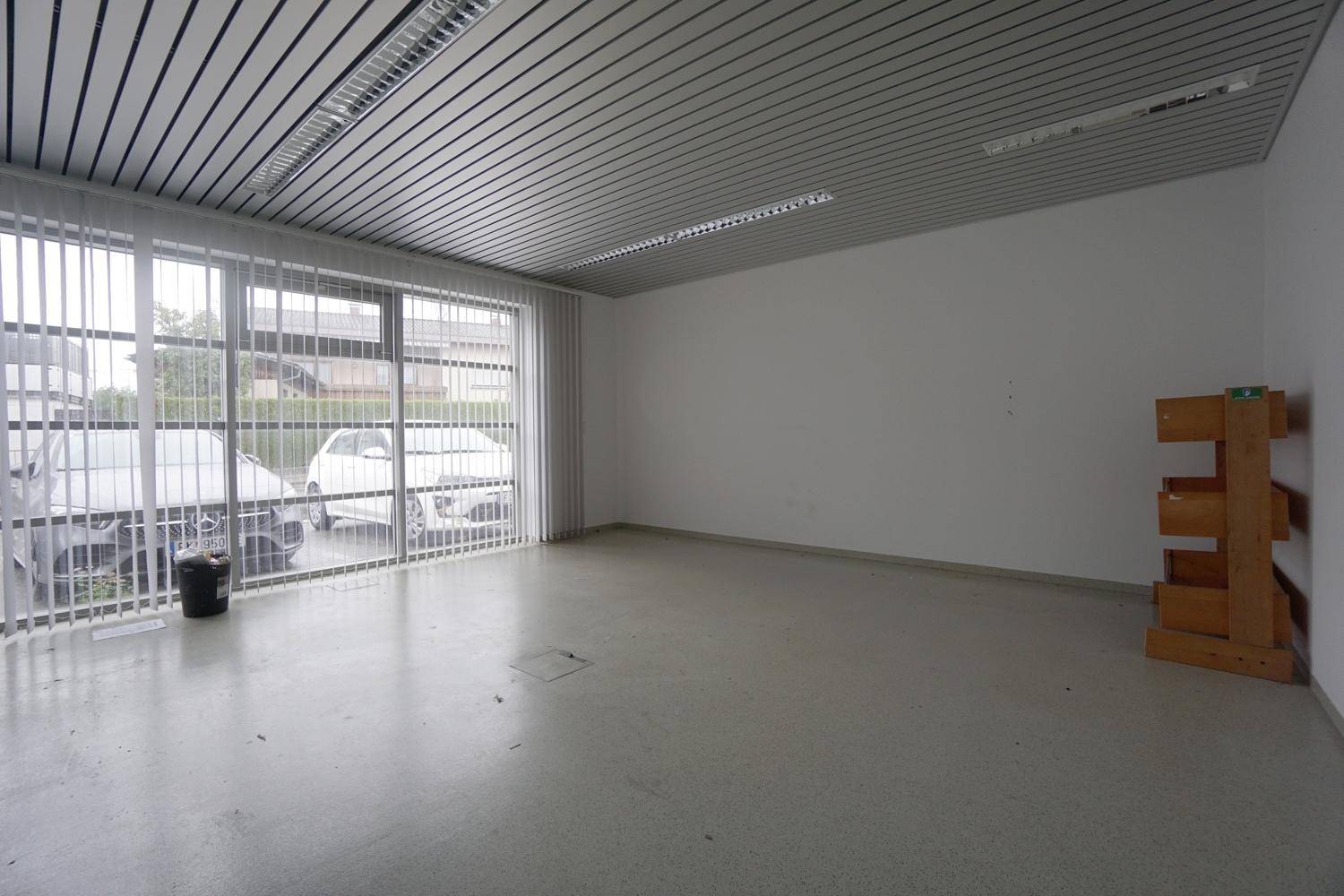 Leerer Büroraum mit großen Fenstern, vertikalen Jalousien und einer modernen Lamellendecke.