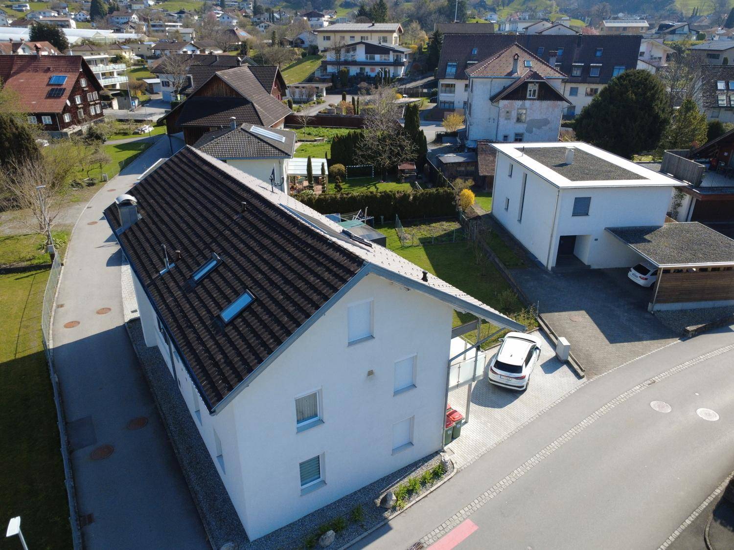 Luftaufnahme des Hauses mit Satteldach, Dachfenstern und umliegenden Wohnhäusern in sonniger Lage.