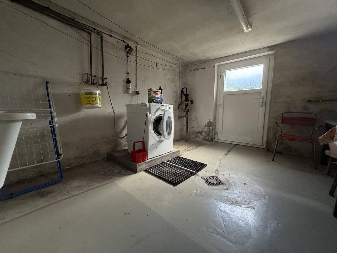 Waschküche im Keller mit Waschmaschine, Waschbecken und Ausgangstür.