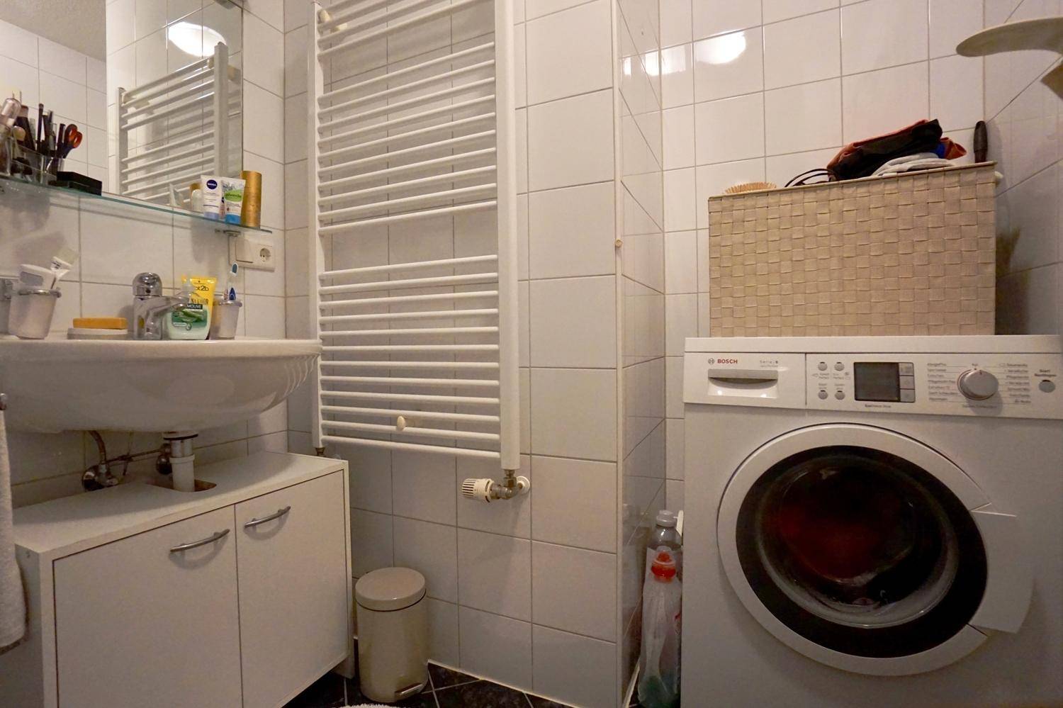 Badezimmer mit Waschbecken, beheiztem Handtuchhalter und Waschmaschine, hell gefliest.